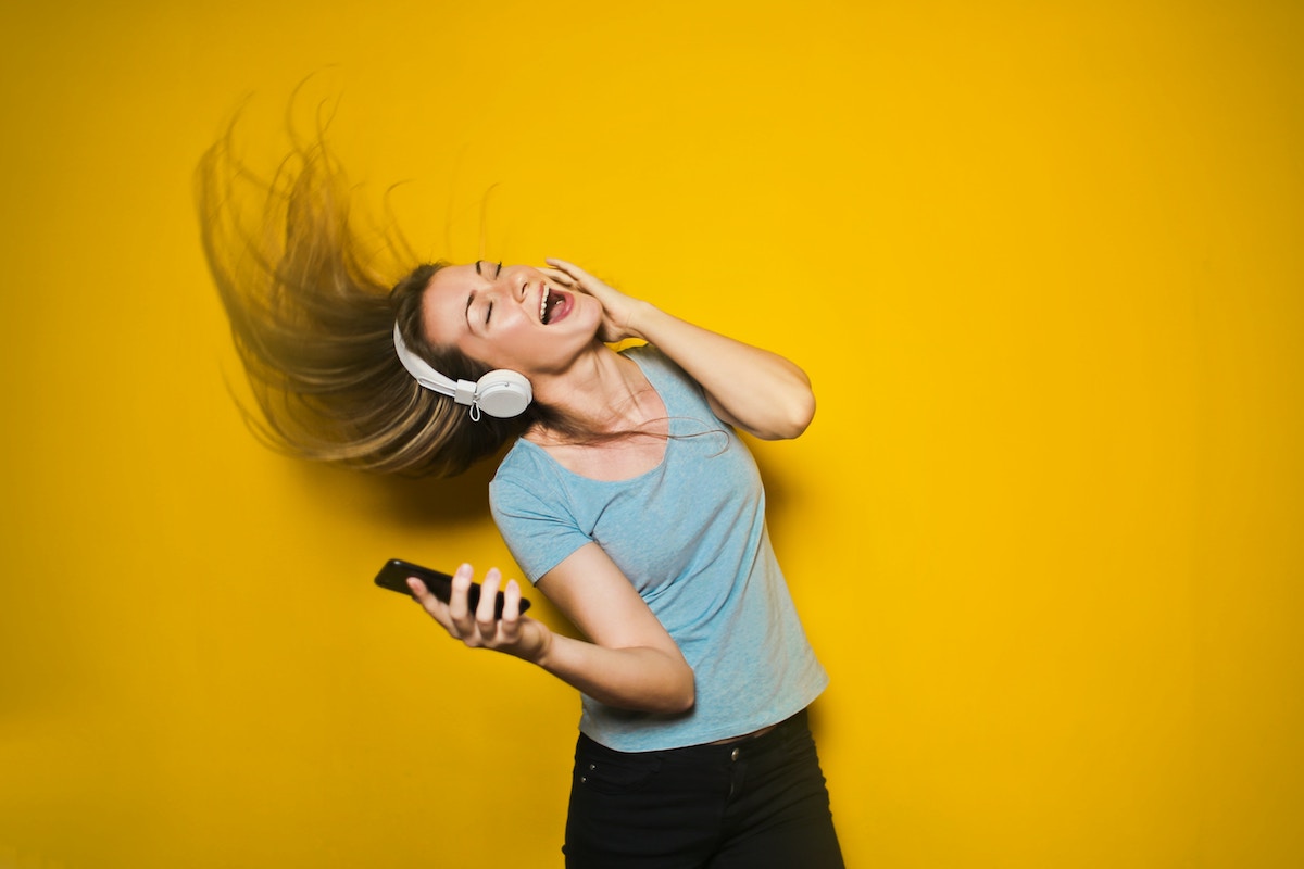Girl listening to headphones and dancing against a yellow wall
