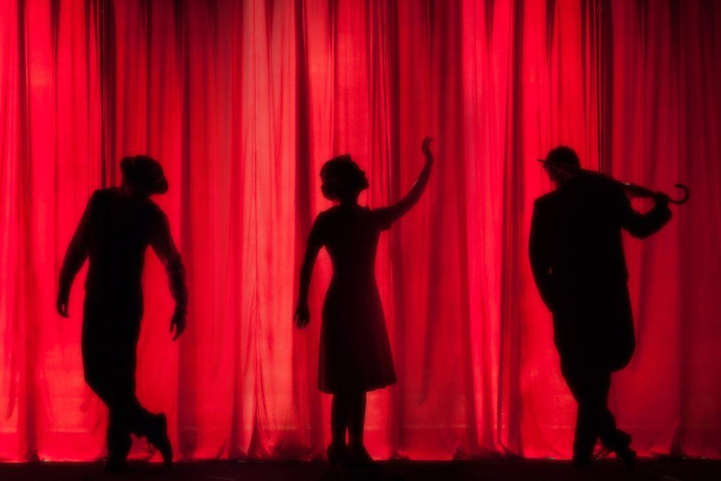 Silhouette of three people against a red curtain