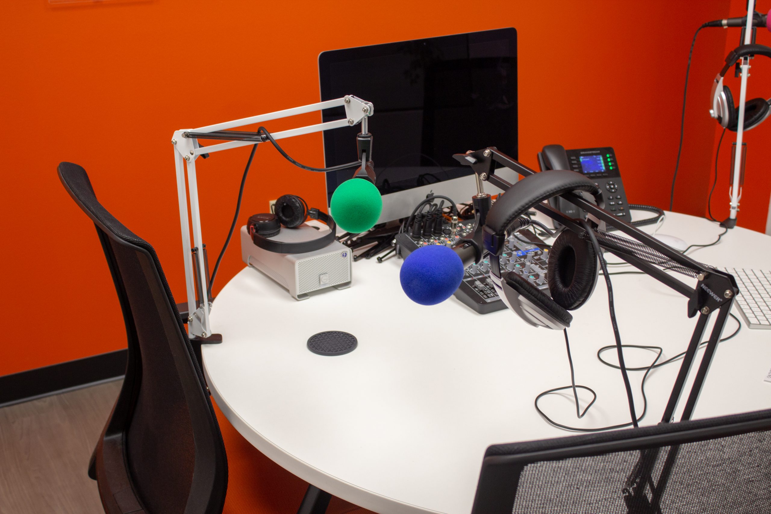 Podcast equipment and Mac on a desk in front of an orange wall